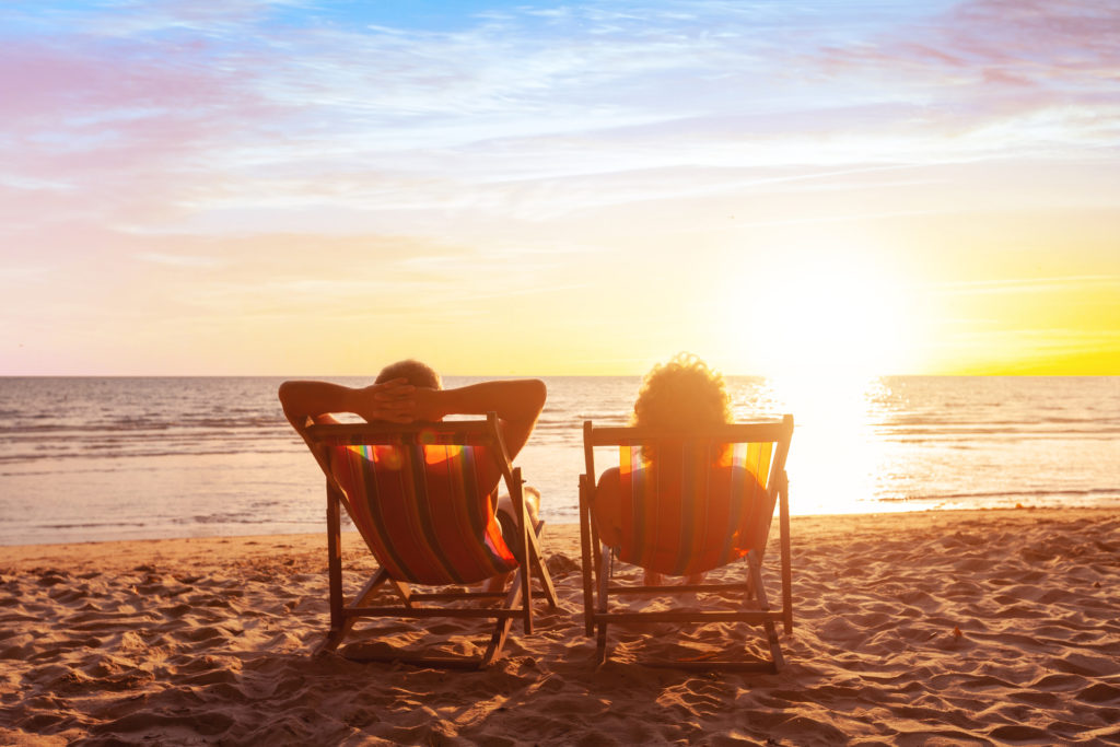 Couple sitting on chairs on a beach at sunset